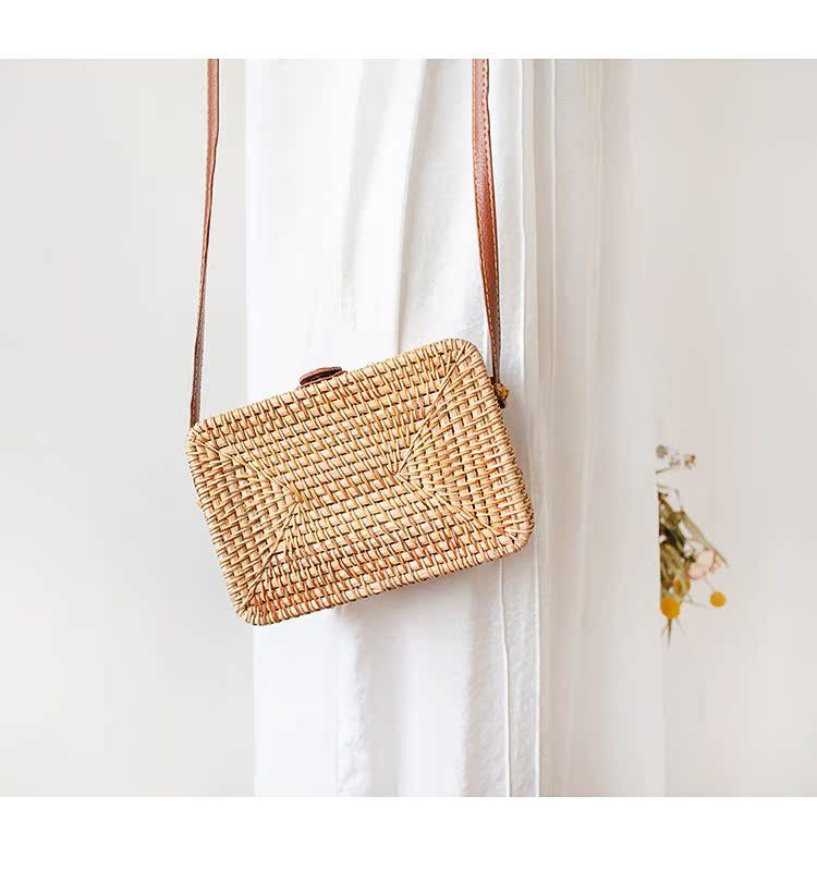 Stylish rattan box bag with natural woven design hanging on a white curtain, featuring a brown strap for casual outings.