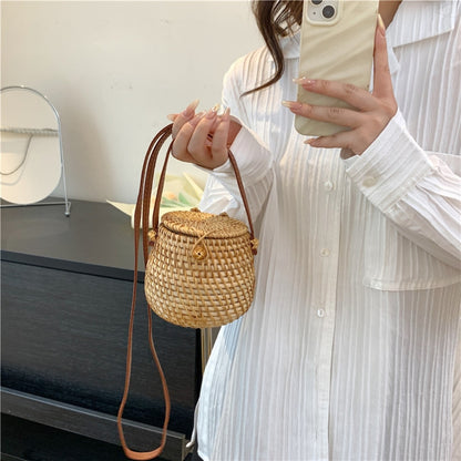 Woman holding handwoven rattan barrel bag with PU leather crossbody strap, boho-chic accessory, eco-friendly and stylish.