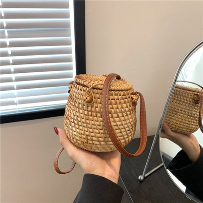 Hand holding eco-friendly rattan barrel bag with PU leather crossbody strap and sturdy woven structure, perfect for boho-chic outfits.